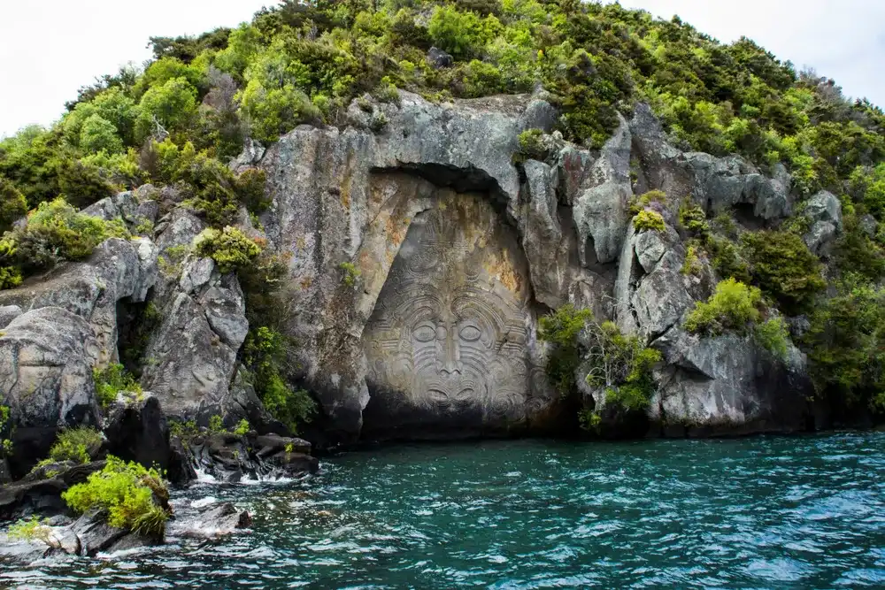 Travel New Zealand, North Island, Taupo. Cruise view of Iconic Maori rock carving in the rock on Great Lake Taupo. Popular tourist attraction/activity. Travel New Zealand, North Island, Taupo. Cruise view of Iconic Maori rock carving in the rock on Great Lake Taupo. Popular tourist attraction/activity.