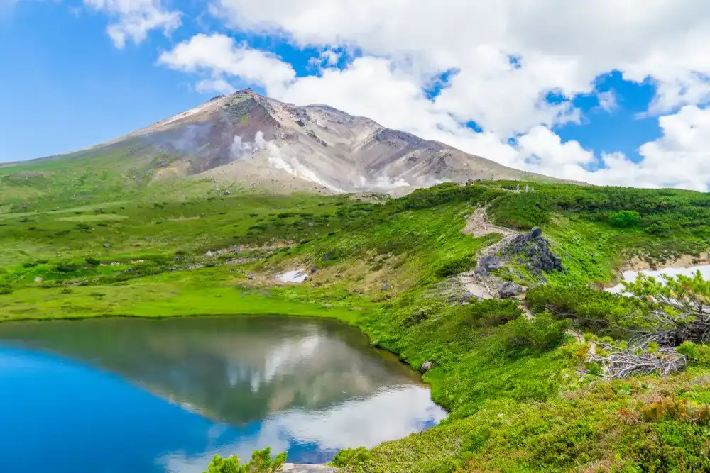 Scenery of Asahidake peak mountain with reflection water and blue cloudy sky in summer, Asahikawa, Hokkaido, Japan. The tallest mountain in Hokkaido and located in the Daisetsuzan National Park Scenery of Asahidake peak mountain with reflection water and blue cloudy sky in summer, Asahikawa, Hokkaido, Japan. The tallest mountain in Hokkaido and located in the Daisetsuzan National Park